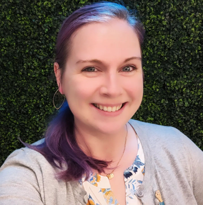 image of Tammi Ramsey, a white woman with purple hair, wearing a flower-print blouse
                    with a grey cardigan against a dark green background